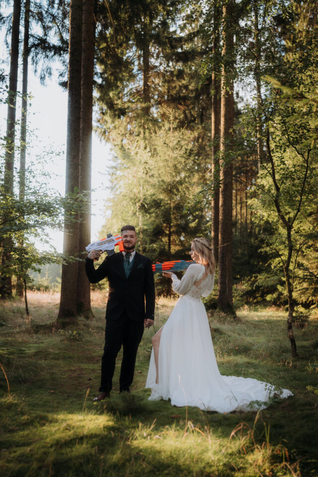 Brautpaar mit Wasserspritzpistole im Wald – witziges Trash-the-Dress-Foto mit Szene-Charakter