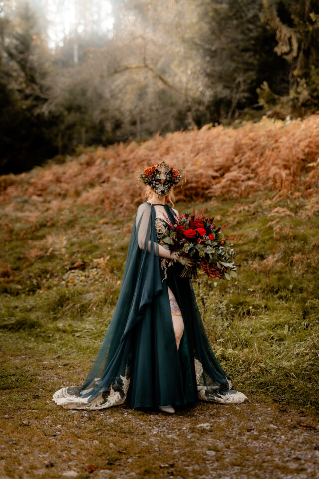 Braut mit Fuchsmaske, gigantischem Brautstrauß und elfenhaftem Kleid in Dunkelgrün - alternative Traumhochzeit im Herbst