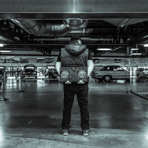 Tom Nawa steht mit DJ-Controller in einer Industrie-Location vor Oldtimern – alternativer Hochzeits-DJ für Paare, die Rock, Metal und Crossover suchen.