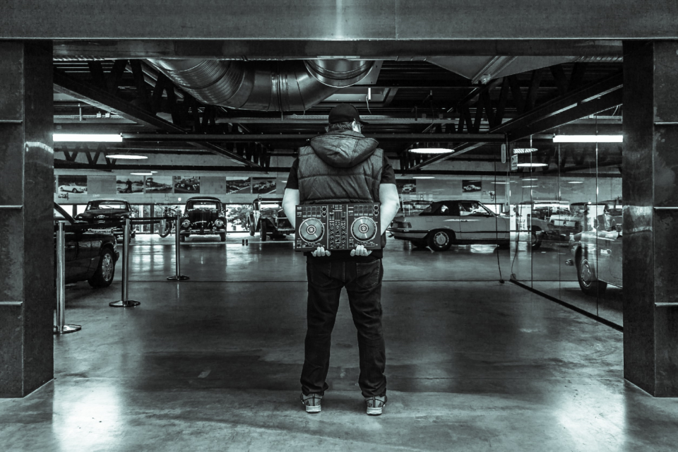 Tom Nawa steht mit DJ-Controller in einer Industrie-Location vor Oldtimern – alternativer Hochzeits-DJ für Paare, die Rock, Metal und Crossover suchen.