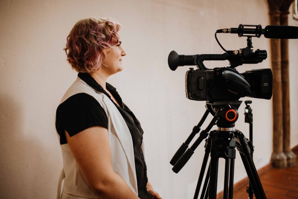 Videofee Johanna Tollkien schaut freundlich zu, während sie eine feenhafte Hochzeit videografiert.