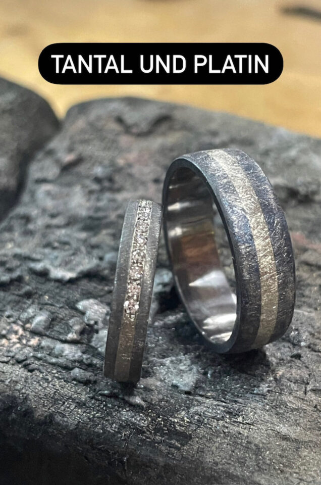 Handgeschmiedete Eheringe mit strukturierter Oberfläche auf dunklem Stein – individuelle Trauringe aus Tantal und Platin für moderne Hochzeiten.