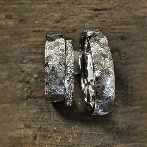 Drei handgeschmiedete Eheringe mit markanter Struktur und feinem Brillantbesatz – individuelle Trauringe aus Silber für moderne, alternative Hochzeiten.