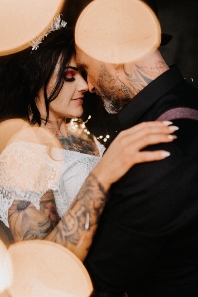 Mystischer Hochzeitsmoment mit dramatischem Make-up und Metal-Vibes – innige Szene eines tätowierten Hochzeitspaars in Close-up.
