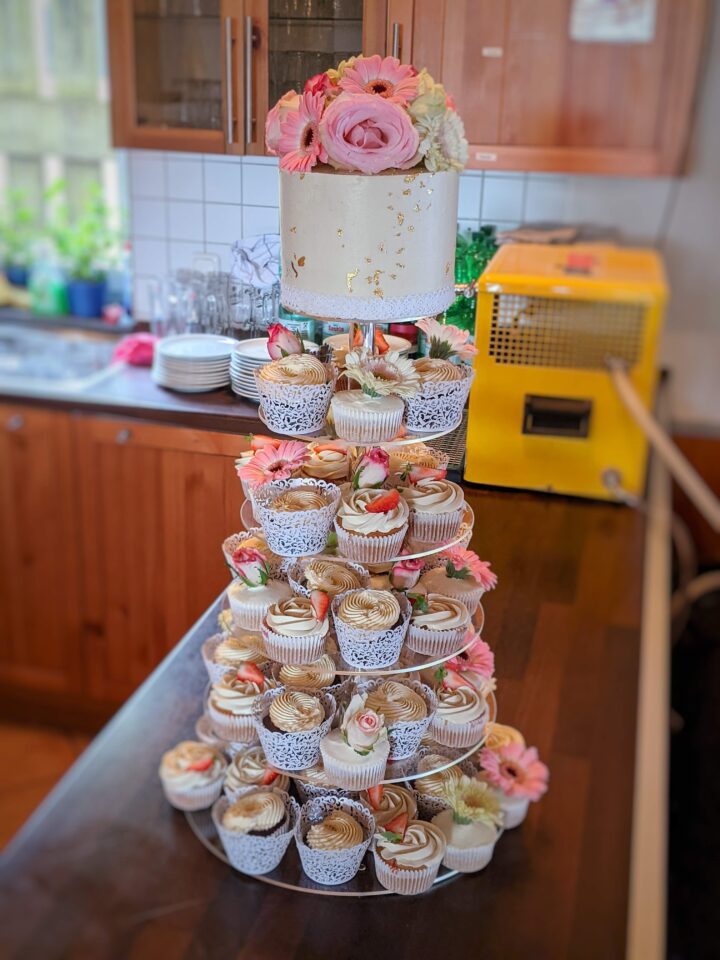 Romantische Hochzeitstorte mit frischen Blumen und Cupcake-Etagere – liebevoll gestaltete Sweet Table-Lösung für moderne Hochzeiten.