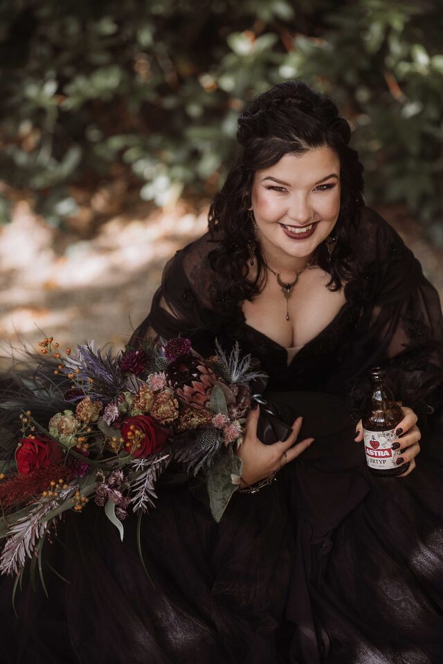 Brautportrait im schwarzen Brautkleid mit üppigem Strauß und Bierflasche – selbstbewusstes Mood-Foto von Patricia Bakker.