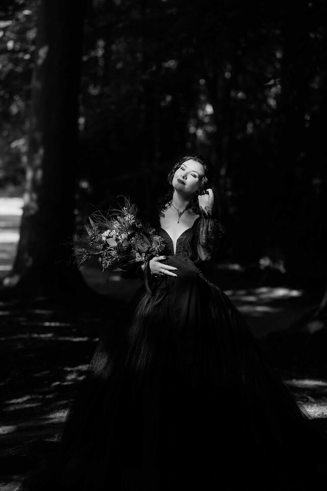 Schwarzweiß-Portrait im Wald: Braut im schwarzen Kleid mit Strauß – fotografiert von Patricia Bakker.