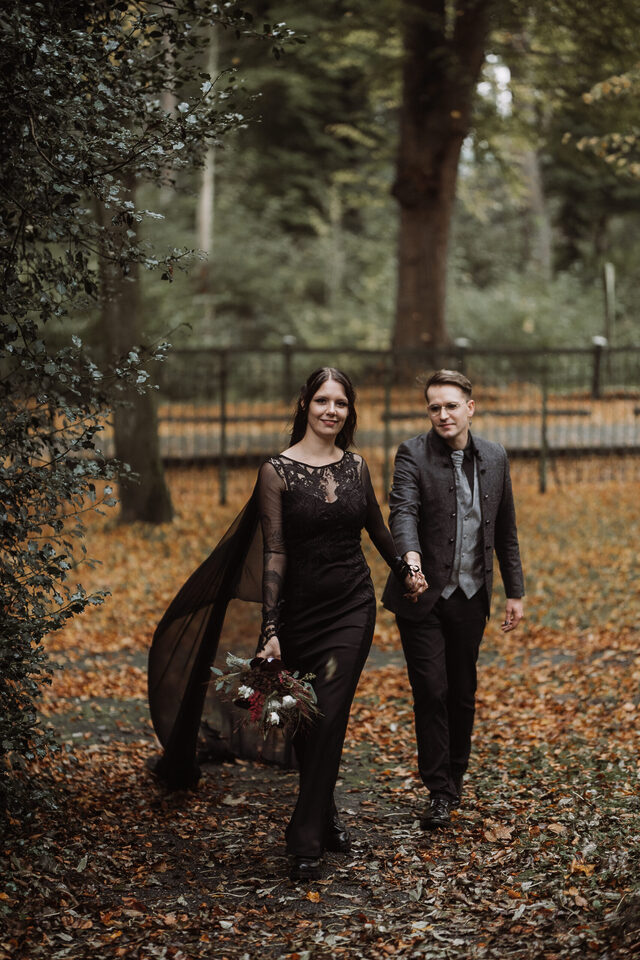 Hochzeitsfotografie von Patricia Bakker: Brautpaar im schwarzen Outfit läuft Hand in Hand durch herbstlichen Park – Paarshooting für alle, die alternativ heiraten.