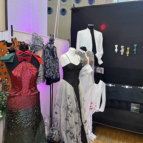 Messestand von Lucky Hardt mit maßgeschneiderter Hochzeitsmode, Kleidern, Anzügen und bunten Accessoires