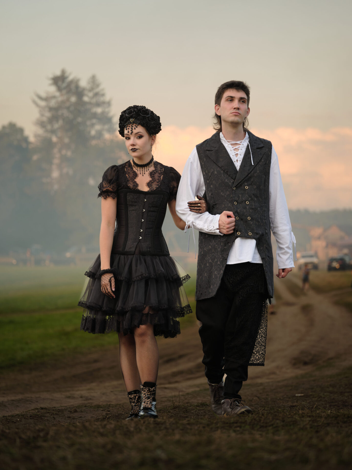 Zwei Personen im Abendlicht, eine im kurzen schwarzen Kleid, die andere mit hellem Hemd, dunkler Weste und Hose