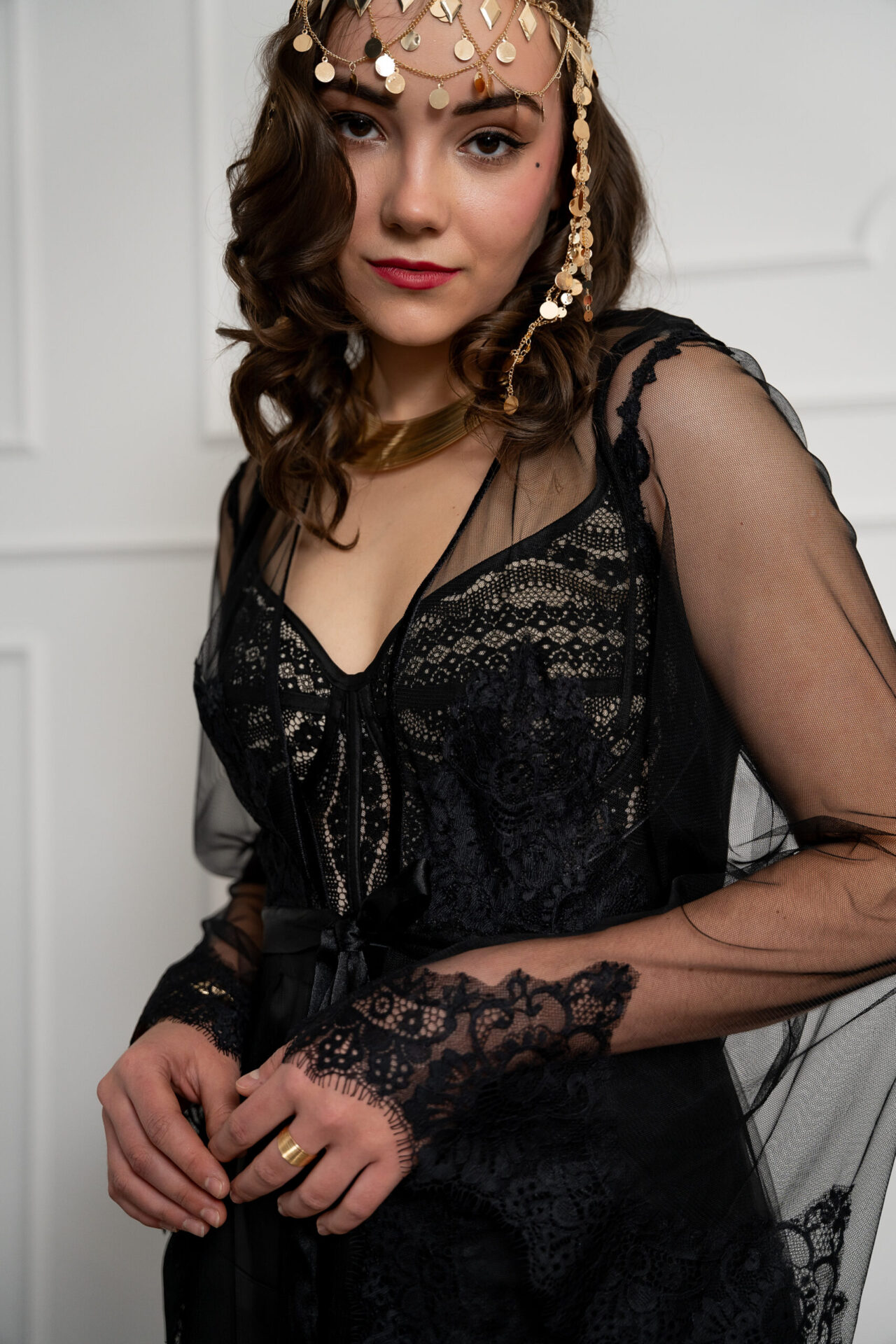 Person in schwarzem Spitzenoutfit mit transparenten Ärmeln und goldfarbenem Stirnschmuck
