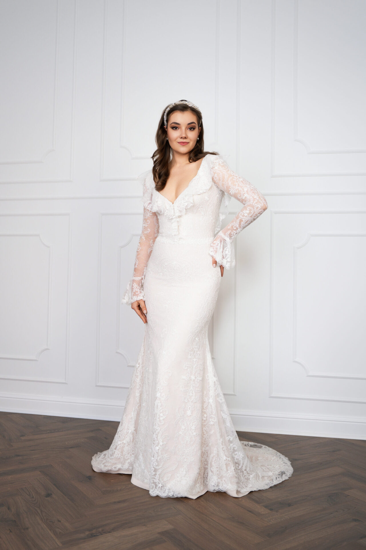Person in langem weißem Spitzenkleid mit transparenten Ärmeln, schmaler Silhouette und ausgestelltem Saum